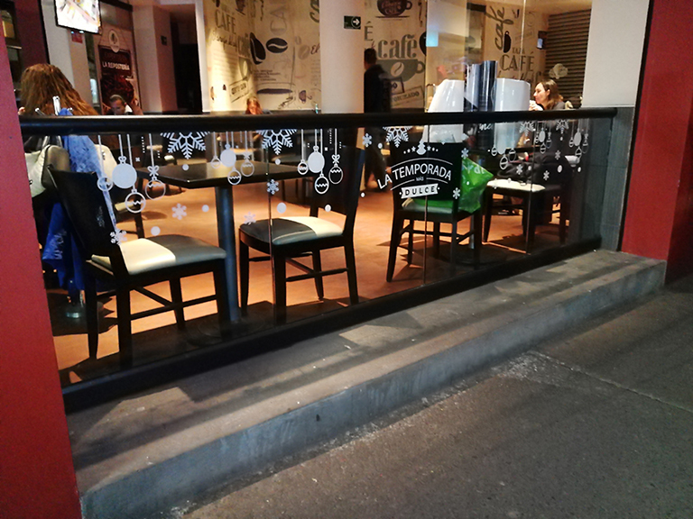 Vinil estático transparente con decoración navideña en barandal de cristal de cafetería en Ciudad de México.